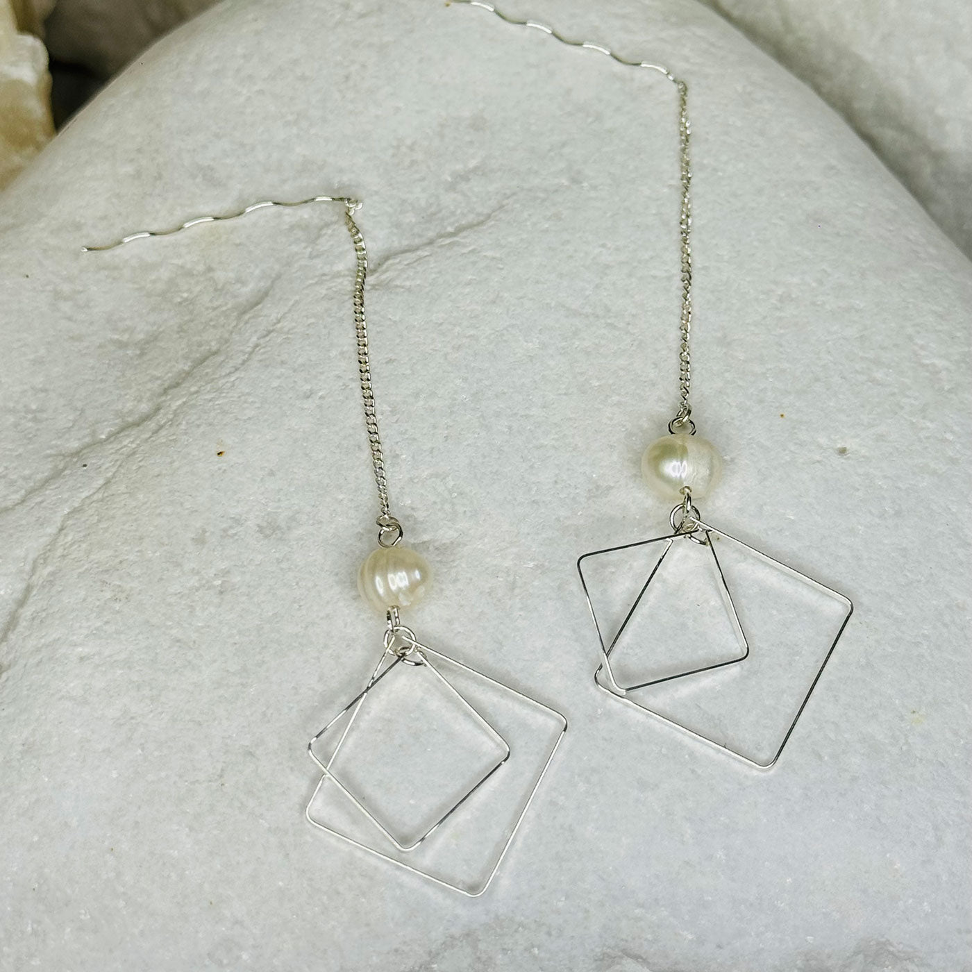 Silver square hoop earrings with pearl beads on a light stone surface